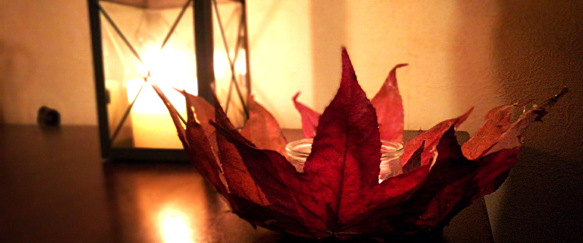 Im Hintergrund ein Windlicht mit brennender Kerze, vorne Herbstdeko in Form einer Laubschale.