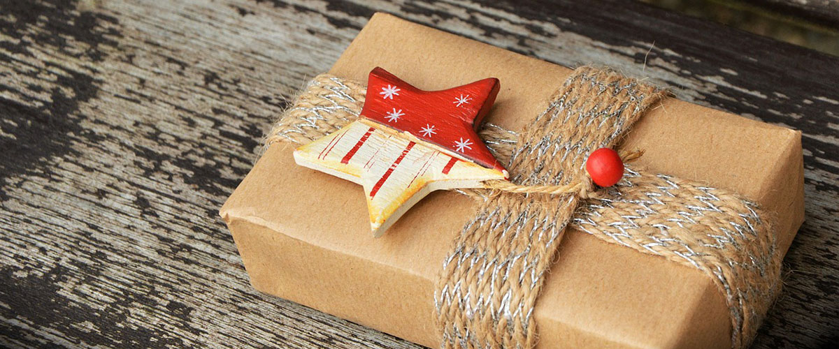 Ein nachhaltig verpacktes Geschenk mit braunem Papier, einer Schleife und einem rot-weißen Holzstern.
