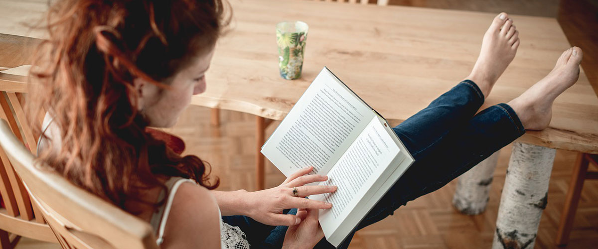 Eine Frau liest mit auf dem Tisch abgelegten Füßen ein Buch.