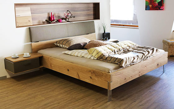Ein Bett aus Holz mit Füßen und ohne Bettkasten. Dies ist das richtige Möbel für Allergiker. Außerdem gibt es einen Holzboden und geschlossene Nachtkonsolen.