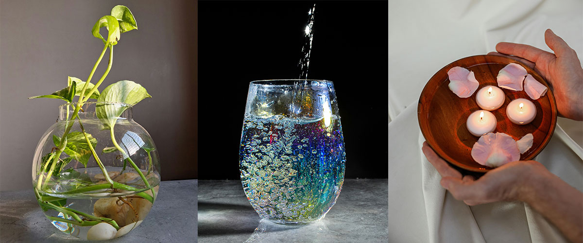 Deko mit Wasser in drei Varianten, eine Pflanze wächst in einem Glas, ein buntes Wasserglas wird befüllt, eine Holzschale mit Wasser, Kerzen und Blüten.